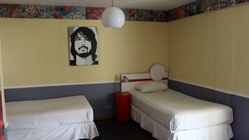 Ein Zimmer mit zwei Einzelbetten, einem roten zylindrischen Gegenstand, einer weißen Pendelleuchte und einer Wand mit einem farbenfrohen Plakat.