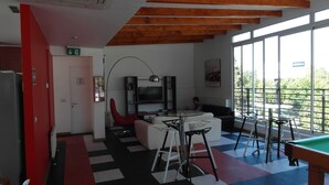 Um interior moderno com mesa de bilhar, uma porta vermelha e uma janela grande.