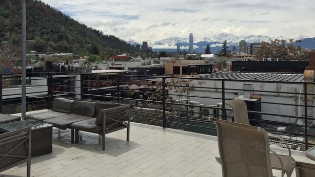 Terraço no telhado com área de estar ao ar livre, vista para a cidade e montanhas ao fundo.