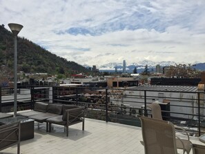 A rooftop terrace with outdoor seating, a view of a cityscape, and mountains in the background. - GUANAKO (Santiago)