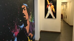 Um corredor com duas obras de arte nas paredes, uma escada ao fundo e chão de azulejos.