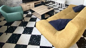 A living room with a checkered floor, a sofa, a chair, a TV, and a patterned wall.