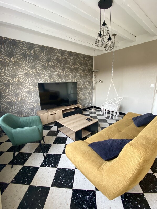 A living room with a checkered floor, a sofa, a chair, a TV, and a patterned wall.