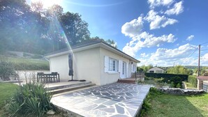 A single-story house with a stone patio, a small outdoor seating area, and a garden.