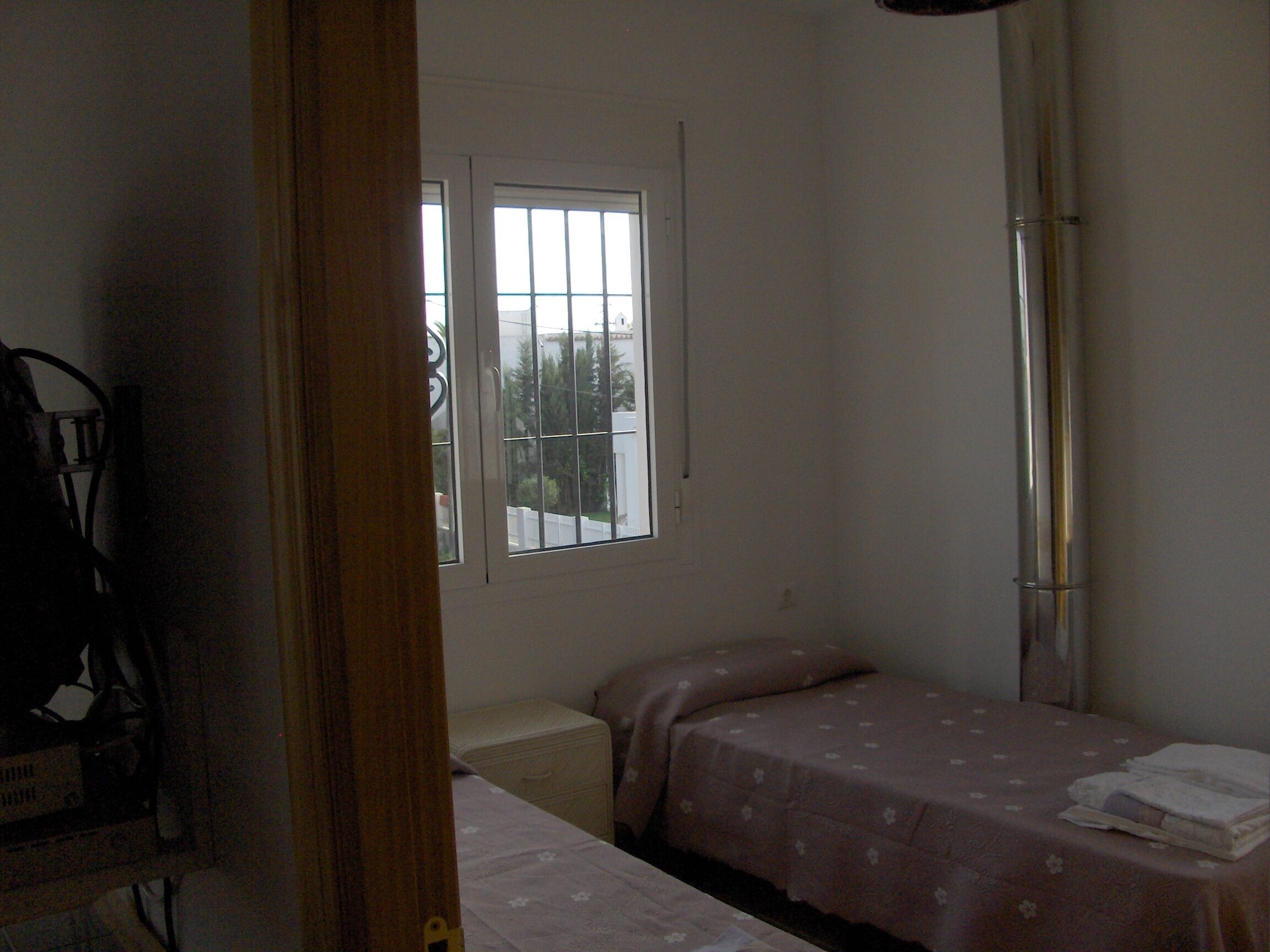A small, sparsely furnished room with a single bed, a window, and a door.
