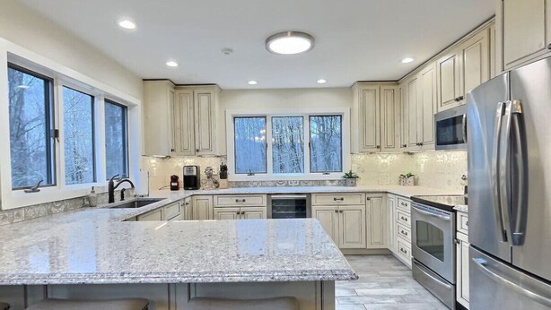 A modern kitchen with a large island, stainless steel appliances, and large windows. - BruinsDen- Hot Tub, Fooseball, Mountain Views (Killington)