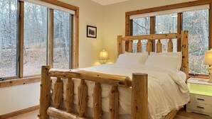 A wooden-framed bed in a room with large windows, a bedside lamp, and a framed picture on the wall. - BruinsDen- Hot Tub, Fooseball, Mountain Views (Killington)