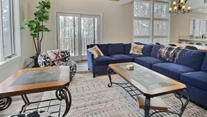 A spacious living room with a blue sofa set, a coffee table, and a large window providing natural light. - BruinsDen- Hot Tub, Fooseball, Mountain Views (Killington)