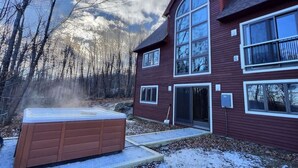 A two-story house with a large window and a hot tub in the front yard. - BruinsDen- Hot Tub, Fooseball, Mountain Views (Killington)