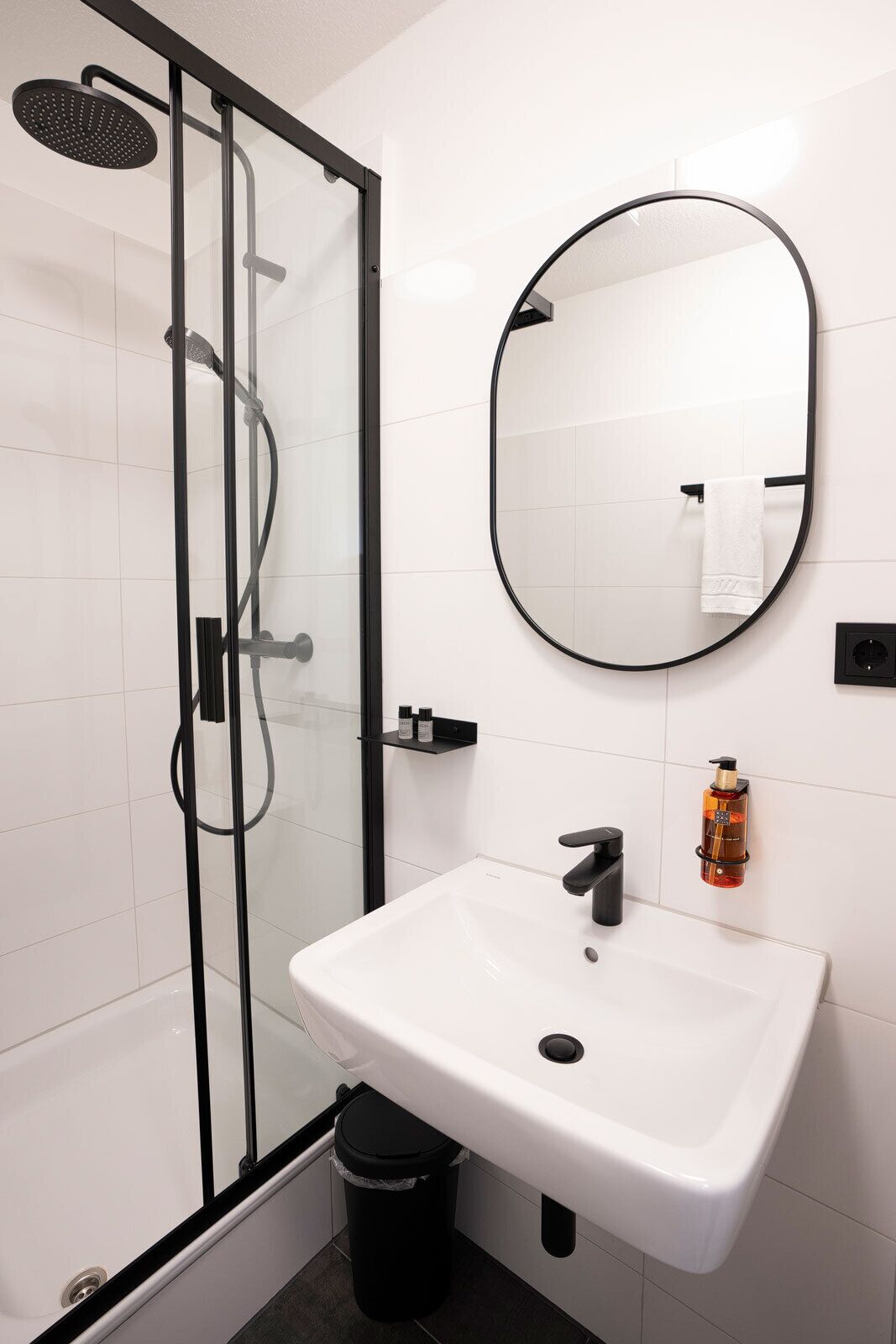 Un baño moderno con ducha envuelta en vidrio, un lavabo blanco y un espejo redondo.