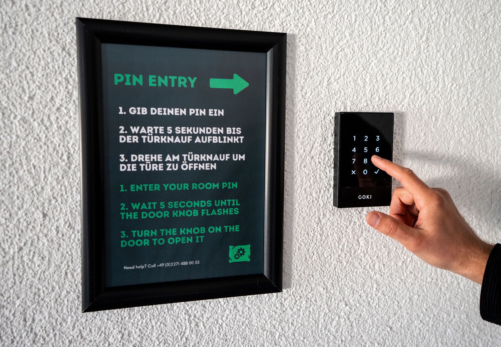 Un panneau d’instructions encadré pour un système d’entrée de porte, doté d’un clavier et d’une main pointant vers celui-ci.