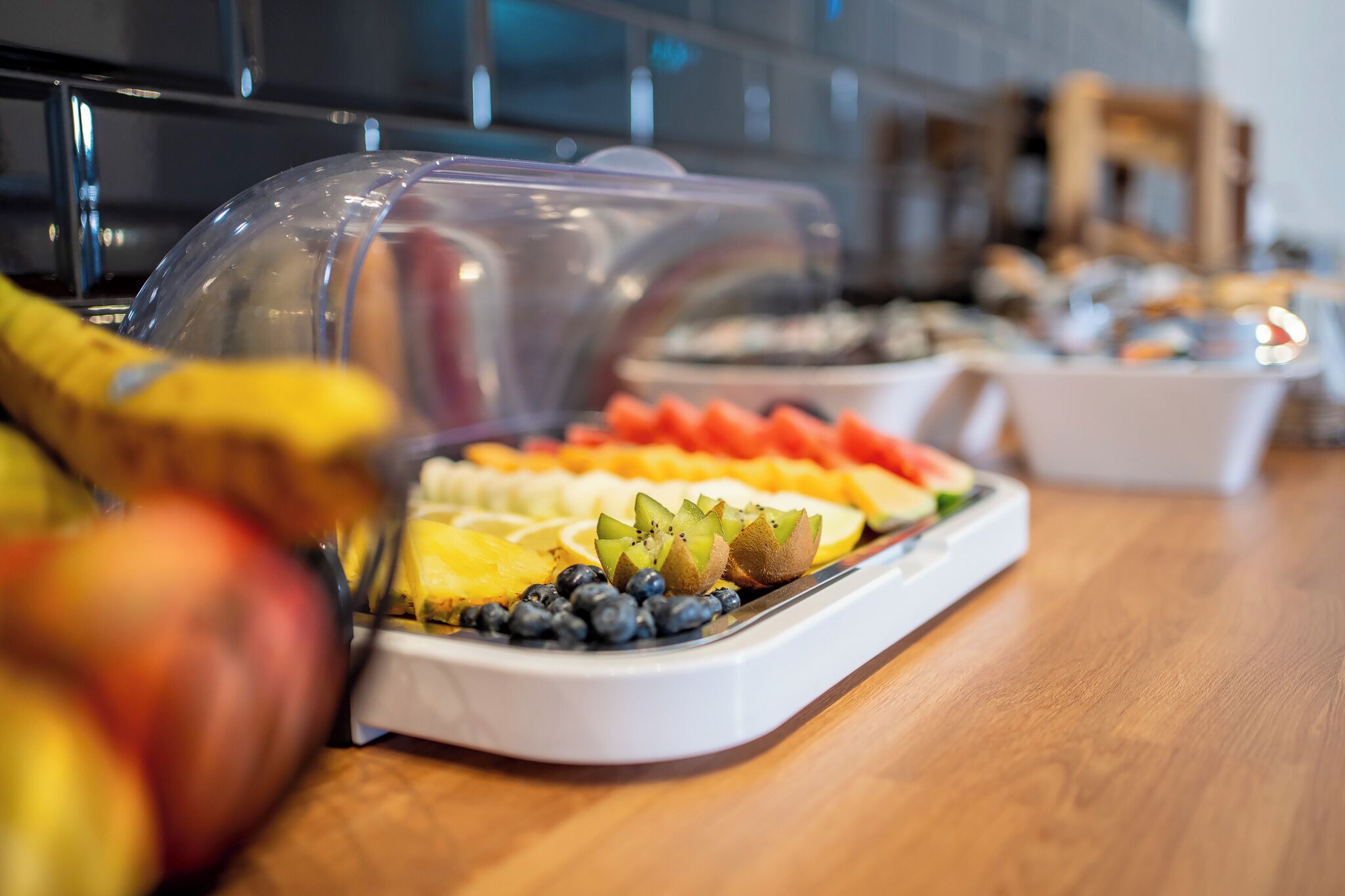 A buffet with various fruits and a clear plastic cover over the food.