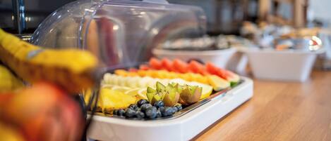A buffet with various fruits and a clear plastic cover over the food.