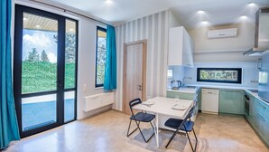 A modern kitchen with a dining area, large windows, and a view of greenery. - H&B apartments Botsvadze (Tbilisi)
