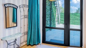 A room with a striped wall, a mirror, a metal shelf, a teal curtain, and a sliding glass door leading to an outdoor area. - H&B apartments Botsvadze (Tbilisi)
