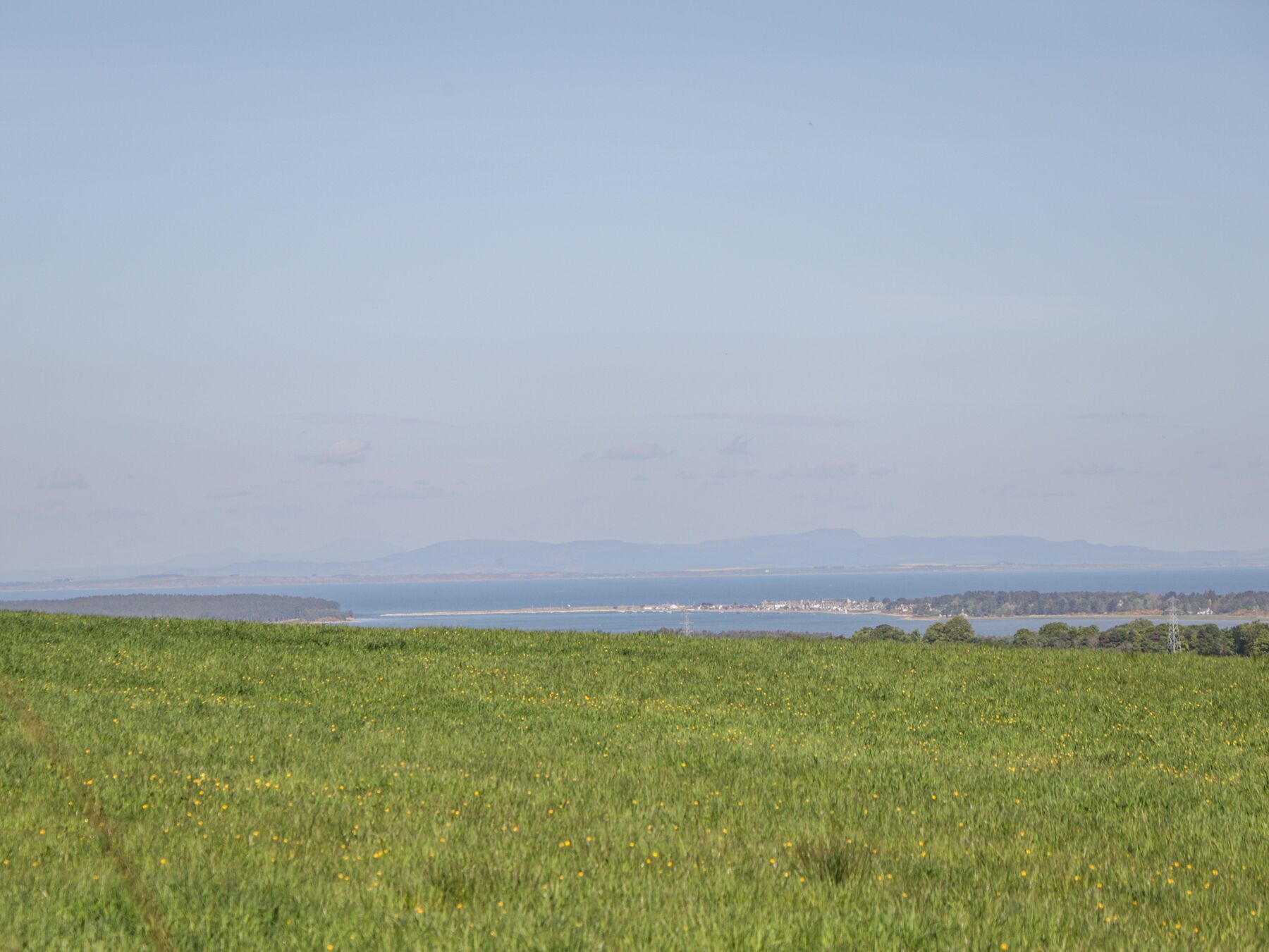A wide, open field with a distant view of a coastline and mountains.