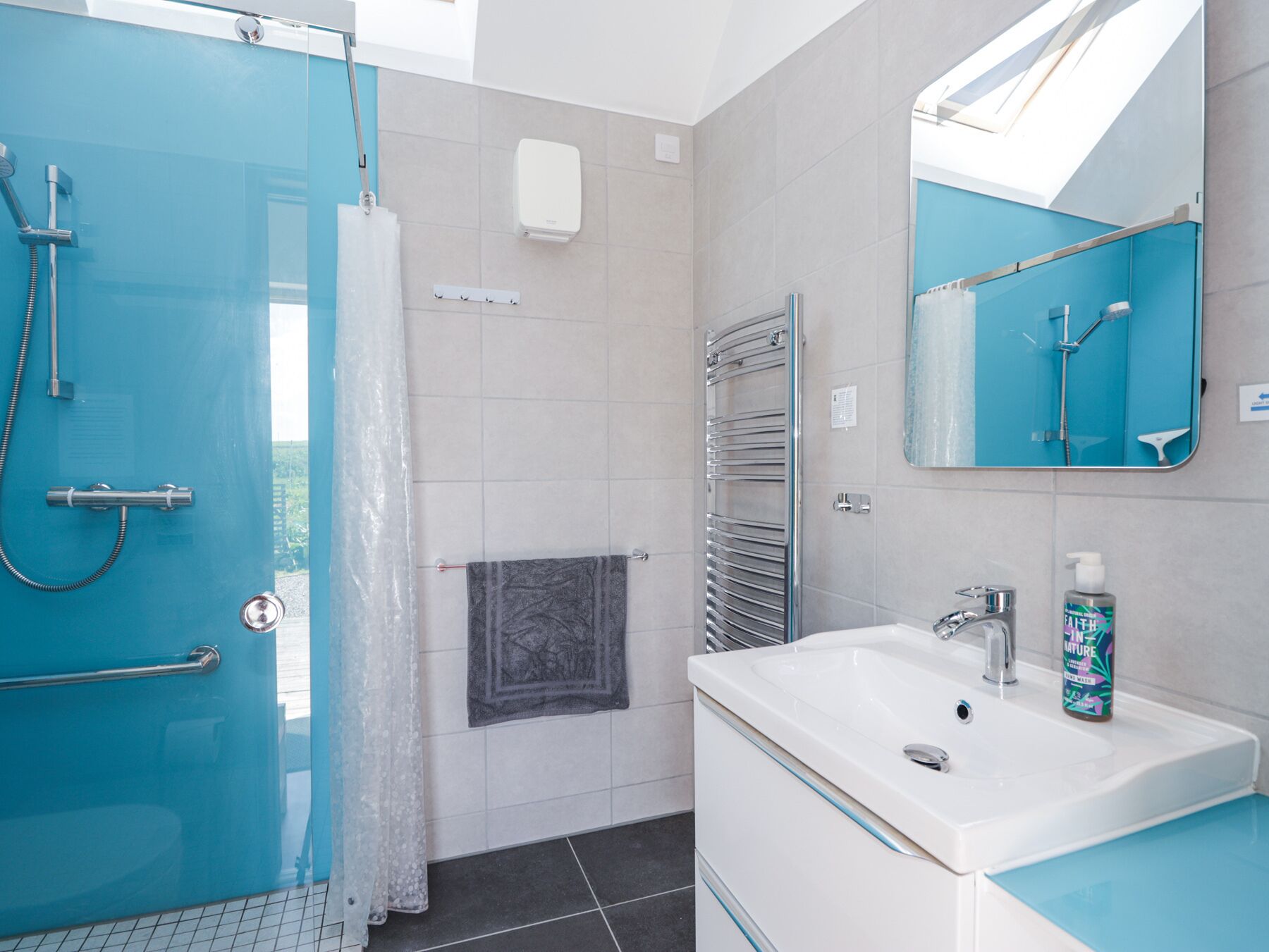 A modern bathroom with a glass shower enclosure, a white sink with a mirror, and a towel rack.