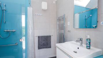 A modern bathroom with a glass shower enclosure, a white sink with a mirror, and a towel rack.
