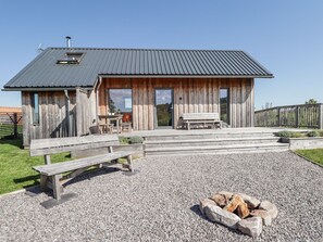 A rustic wooden cabin with a metal roof, a wooden deck, a bench, and a fire pit.