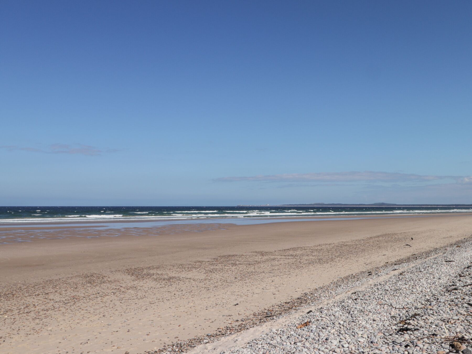 Ein weiter Sandstrand bei blauem Himmel.