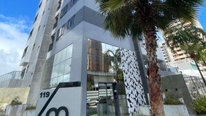 Un edifici alt i modern amb una façana geomètrica característica, una palmera al primer pla i un rètol amb un número de edifici.