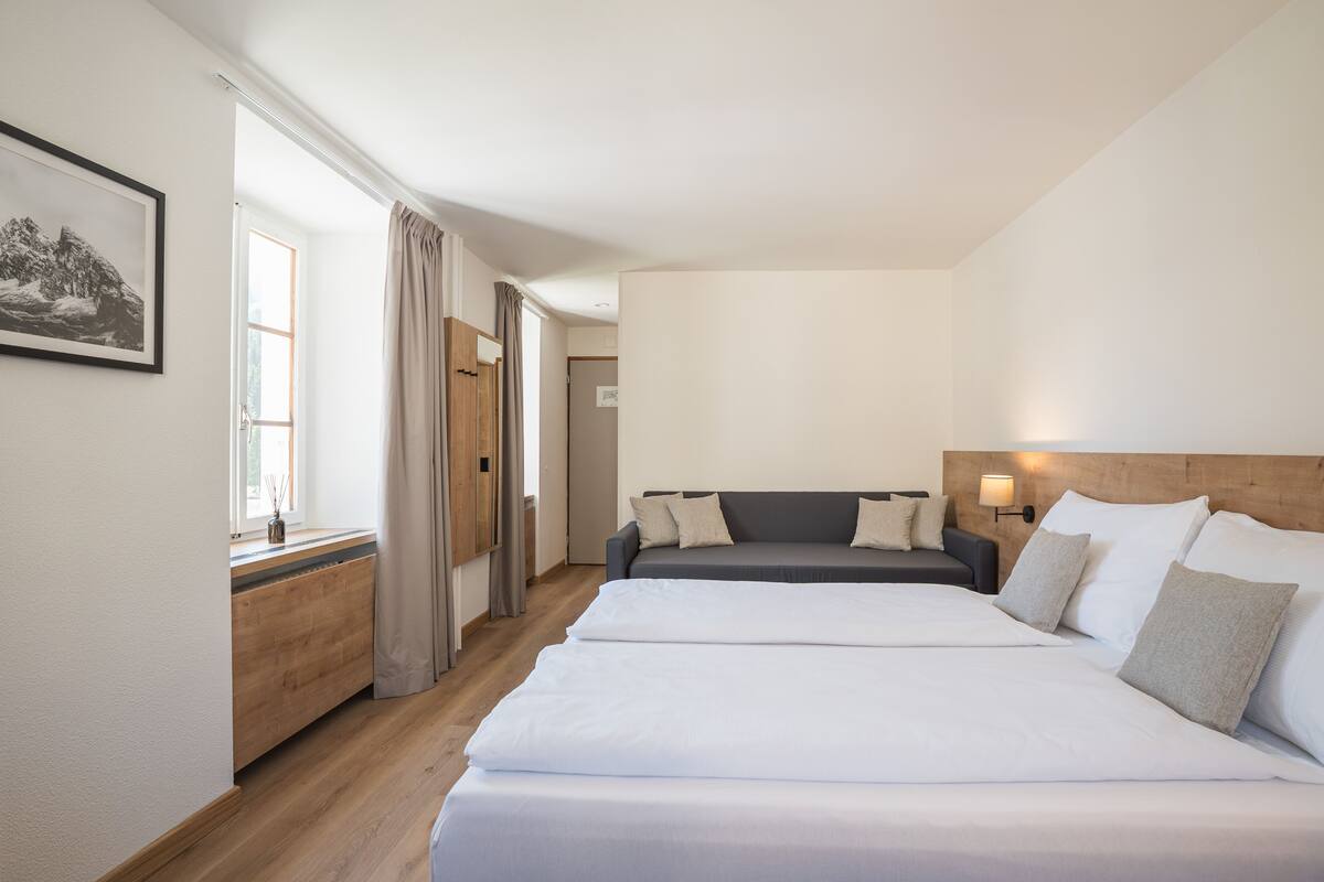 A hotel room with two beds, a wooden dresser, a window with curtains, and a framed picture on the wall.