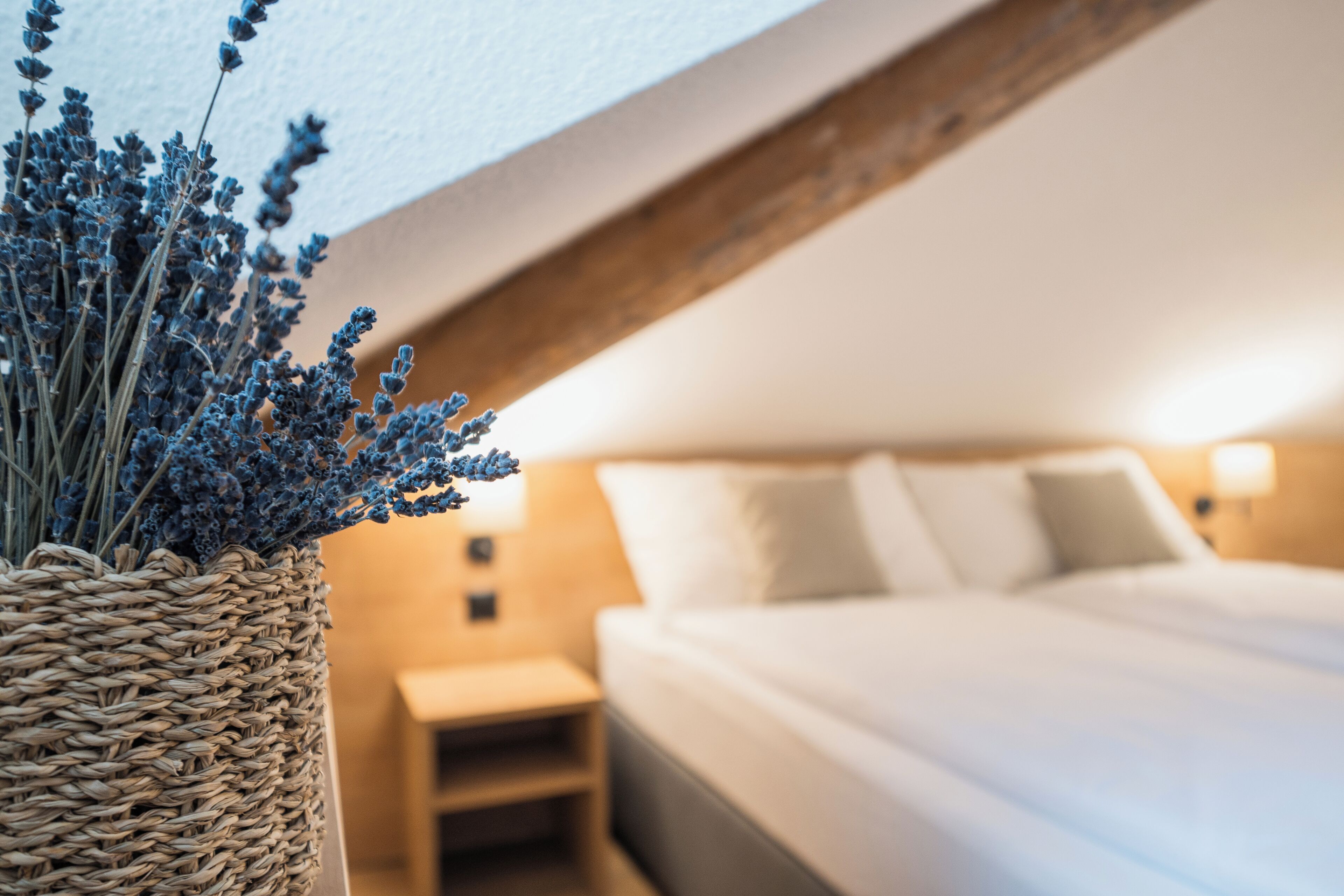 Een slaapkamer met een bed, nachtkastje en een geweven mand met lavendel.