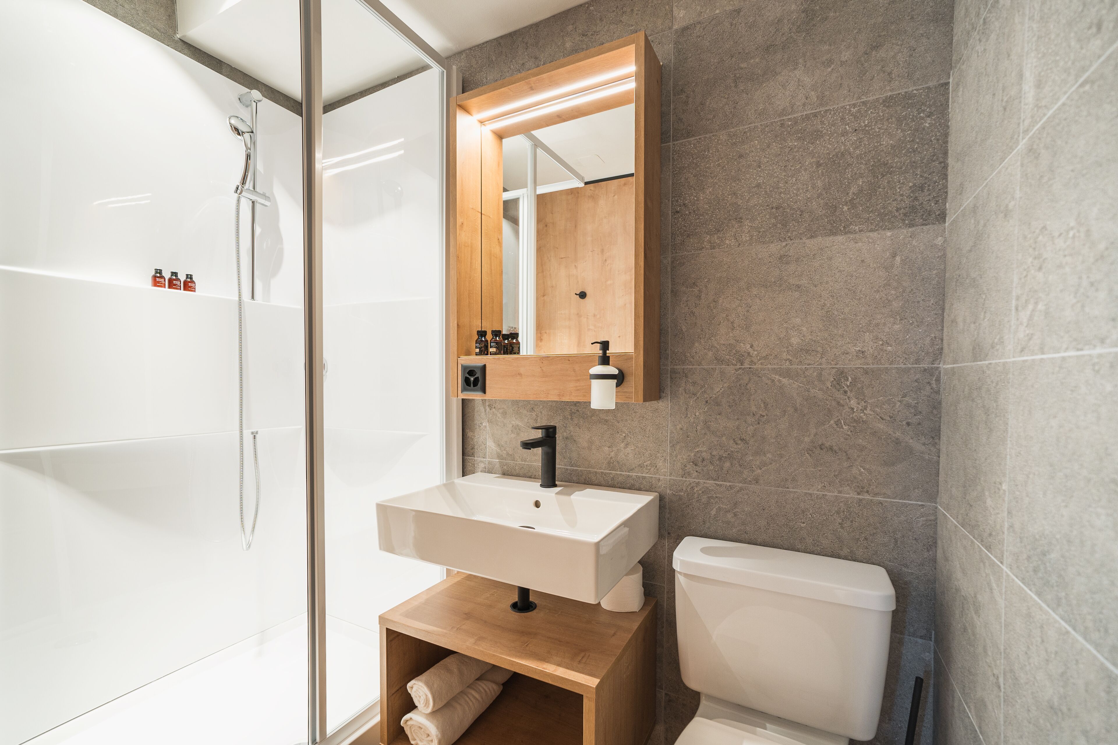 Ein modernes Badezimmer mit Duschkabine aus Glas, einem Holzwaschtisch mit weißem Waschbecken und einer Toilette.