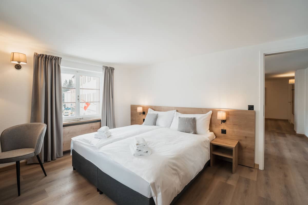 A hotel room with a large bed, bedside tables, a chair, and a window with curtains.