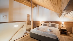 A modern bedroom with a wooden ceiling, a large bed with neatly folded towels, two bedside tables, and a wooden nightstand.