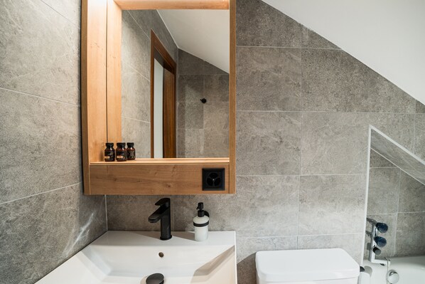 Un baño con lavamanos blanco, espejo y zona de ducha.