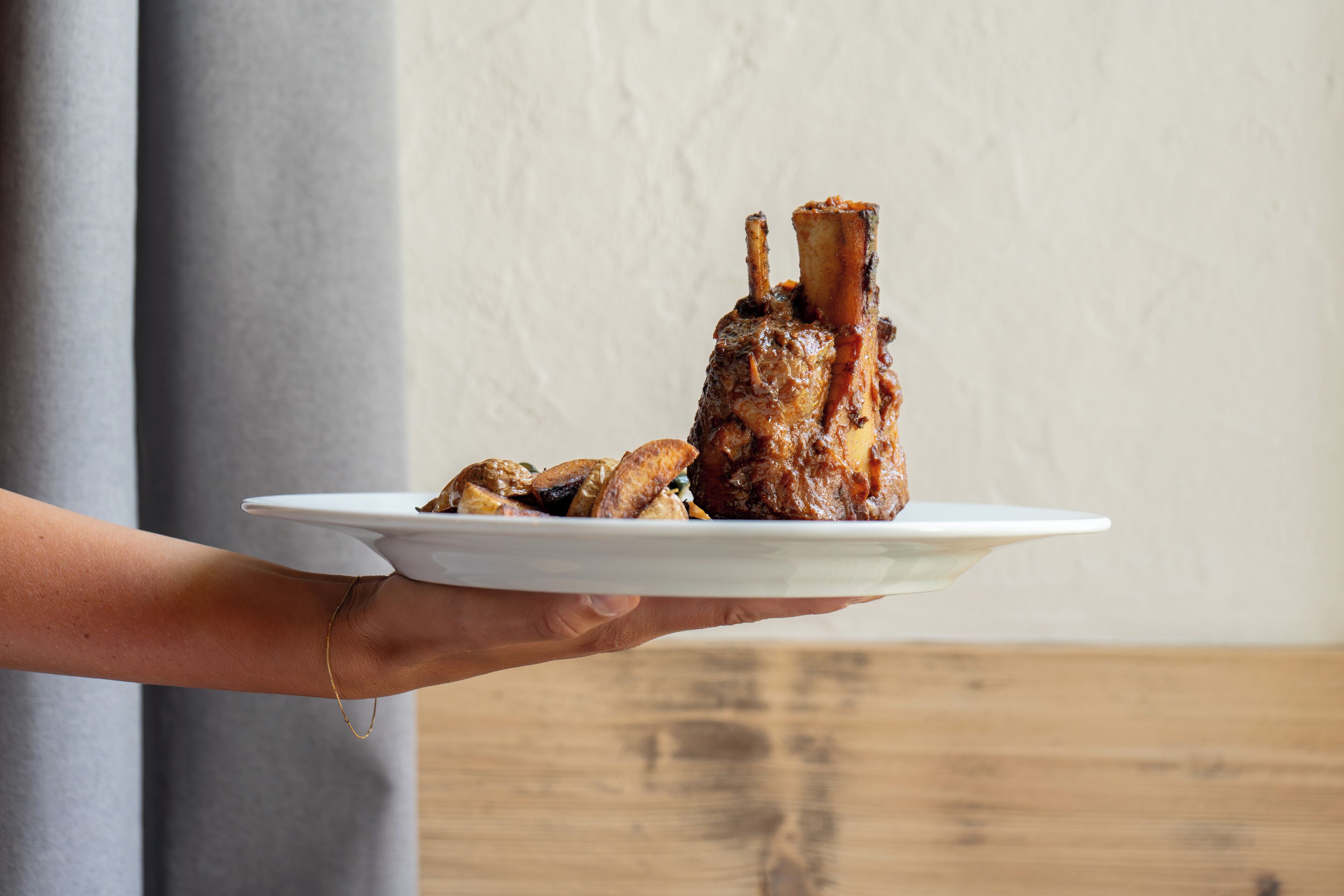 Una persona sosteniendo un plato con un palillo de cordero asado y setas.