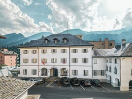 Un edificio con fachada blanca, múltiples ventanas e una bandera en la parte superior. Hay coches aparcados adelante.