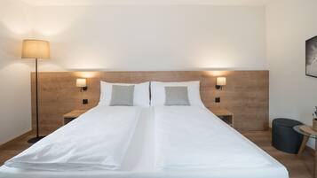 Ein ordentlich gemachtes Bett mit weißen Leinentüchern, zwei Nachttische mit Lampen, ein Holzkopfende und ein kleiner runder Tisch mit einem Korb.