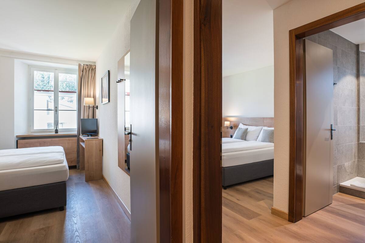 A hotel room with two beds, a desk, a TV, and a window with curtains.