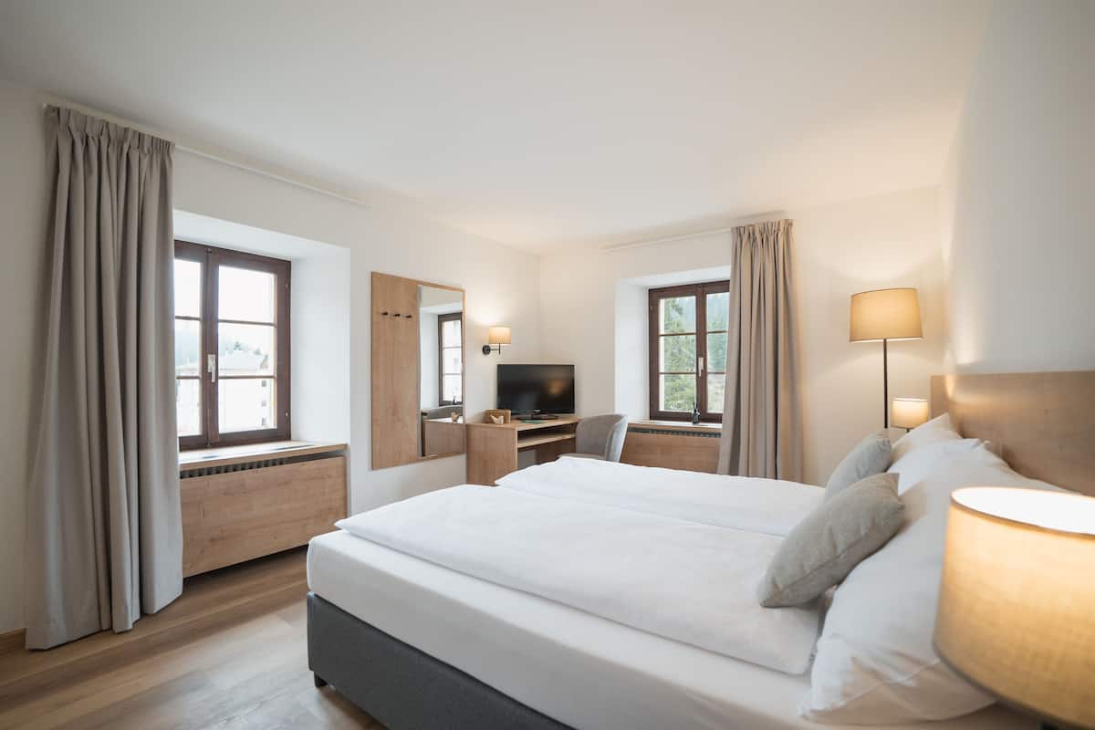 A hotel room with a large bed, a desk with a computer, a TV, and a window with curtains.