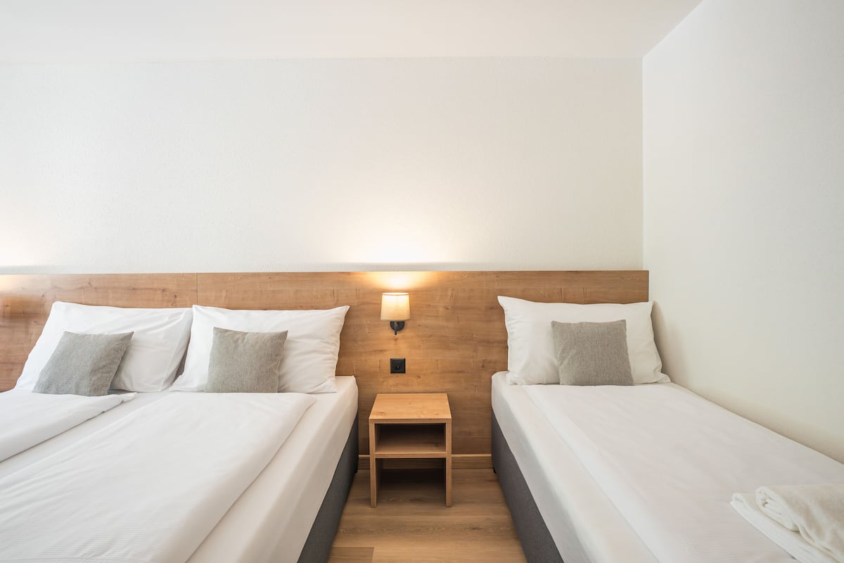 A hotel room with two beds, a nightstand, and a wall-mounted lamp.