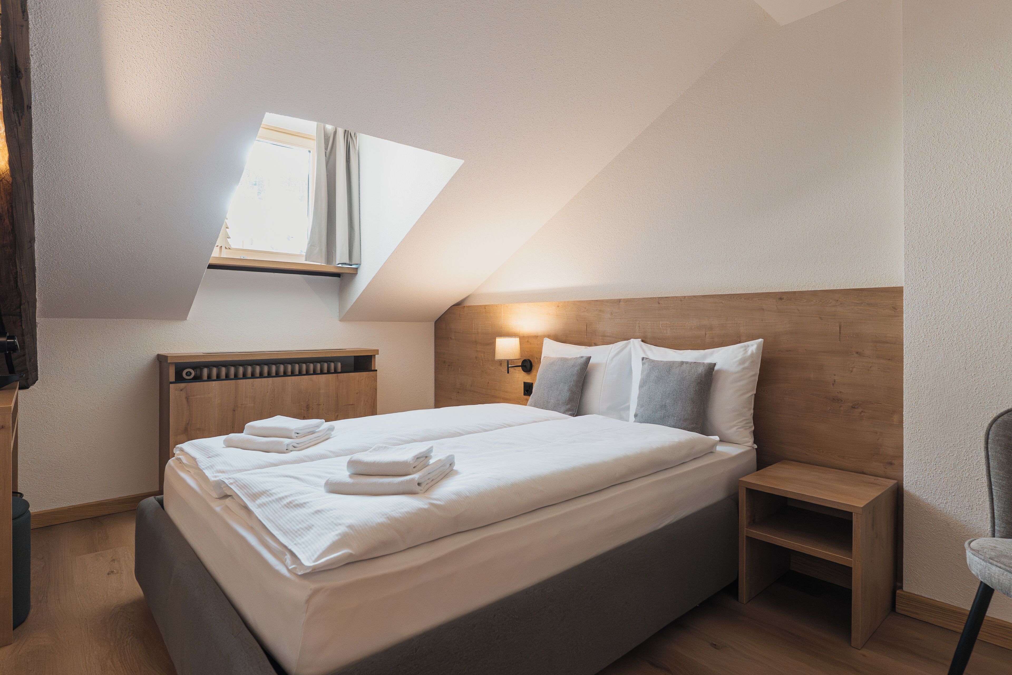 Ein Schlafzimmer mit Bett, Nachttisch, Lampe und Fenster.