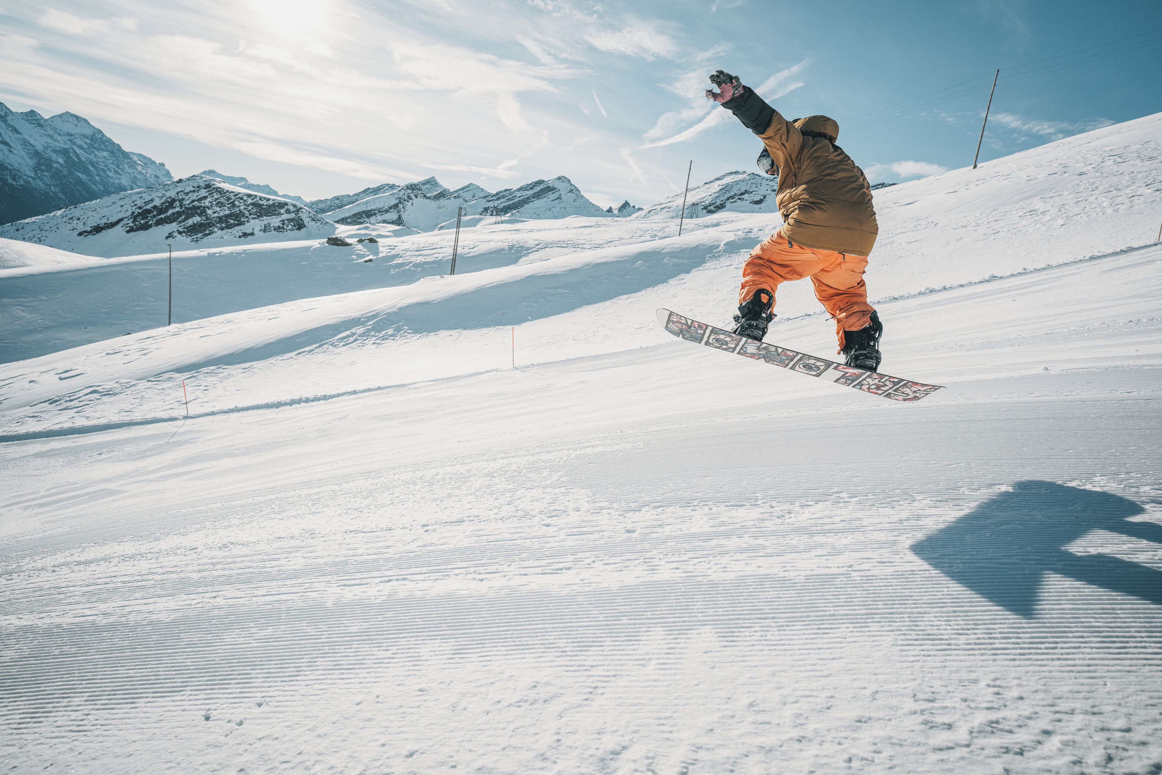 Un snowboarder en pleno vuelo sobre una pendiente nevada, con montañas al fondo.