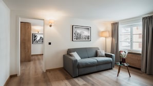 A living room with a grey sofa, a glass coffee table, a framed picture on the wall, and a lamp.