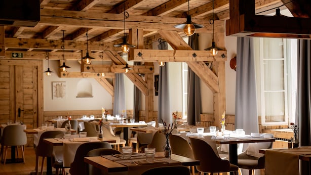 A restaurant with wooden beams, hanging pendant lights, and tables set for dining.