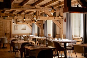 Un restaurante con vigas de madera, lámparas colgantes y mesas dispuestas para comer.