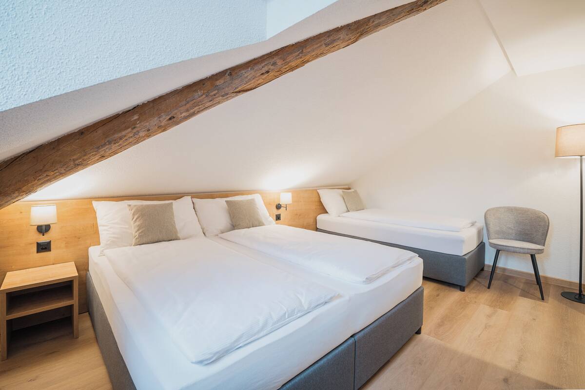 A modern bedroom with two beds, a wooden ceiling, a nightstand, and a chair.