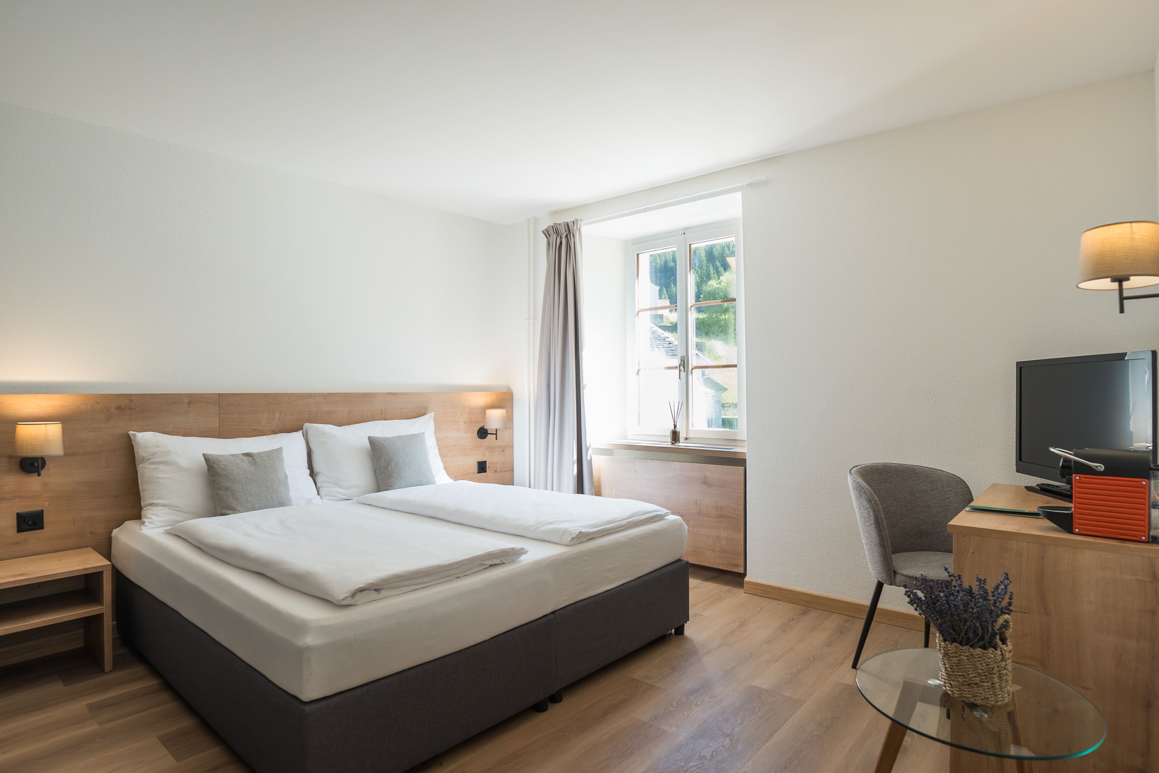 Una habitación de hotel moderna con una cama grande, televisión, escritorio y ventana con cortinas.