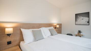Ein ordentlich bezogenes Bett mit weißen Leinentüchern und zwei Kissen, ein hölzerner Kopfteil, eine Wandlampe und ein gerahmtes Bild an der Wand.