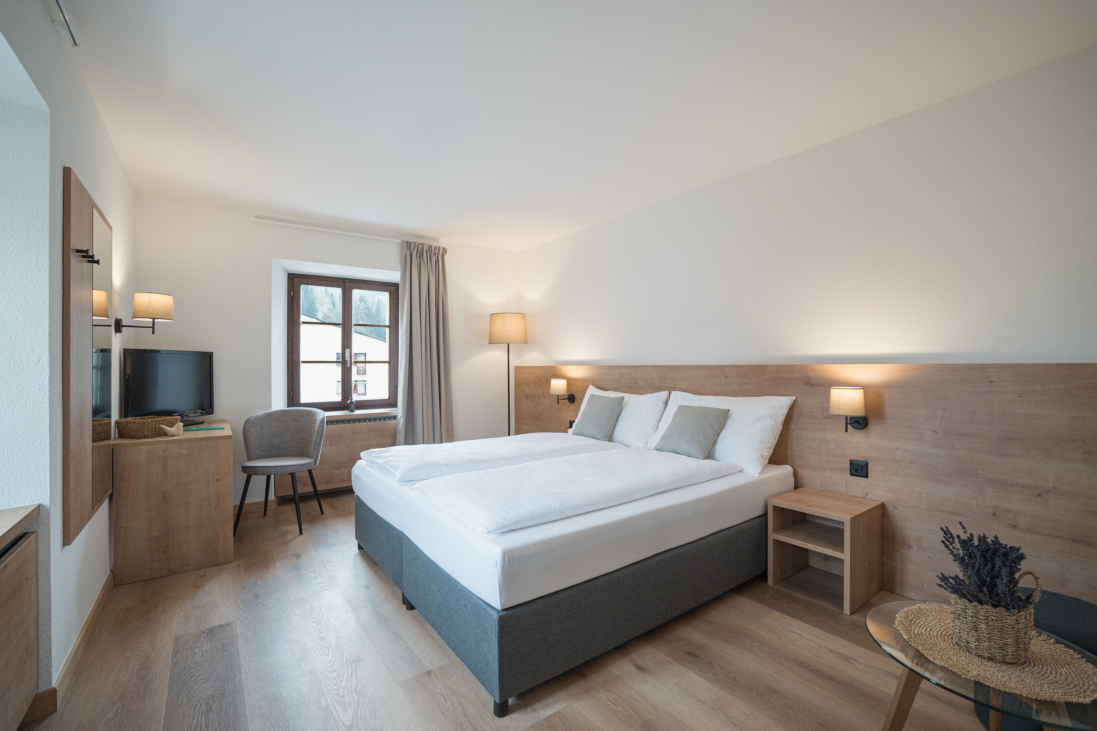 Een moderne hotelkamer met een groot bed, een bureau, een stoel, een televisie en twee bedlampjes.