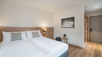A modern hotel room with a large bed, a small side table, a wall-mounted lamp, and a framed picture on the wall.