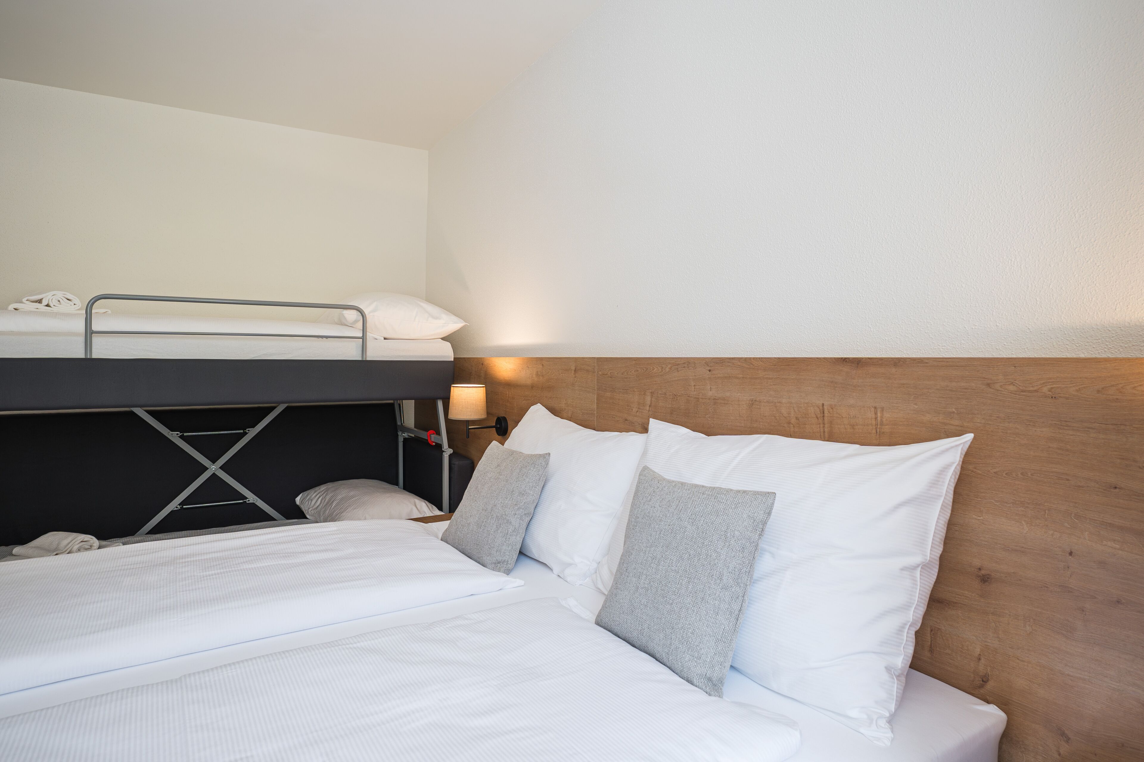 A hotel room with a bunk bed, a wooden headboard, and a bedside table with a lamp.