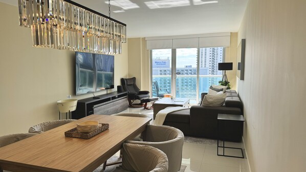 Una sala moderna con comedor, un ventanal con vista a la ciudad, un sofá de cuero negro y una mesa de comedor de madera.