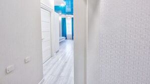 Een hal met een witte deur, een bed met blauwe gordijnen en een behang met patroon.
